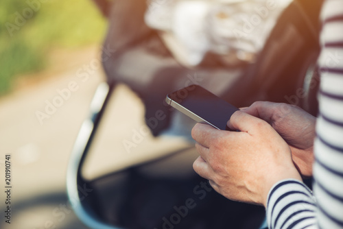 Mother using mobile phone by the baby stroller