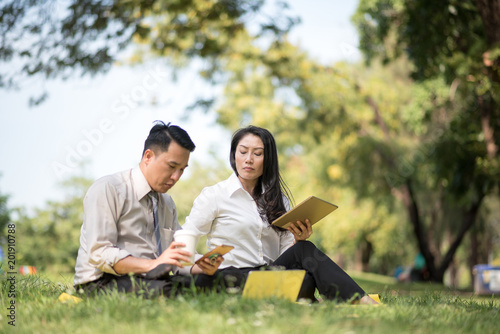 Selective focus business couple relaxing with tablets in park after work done