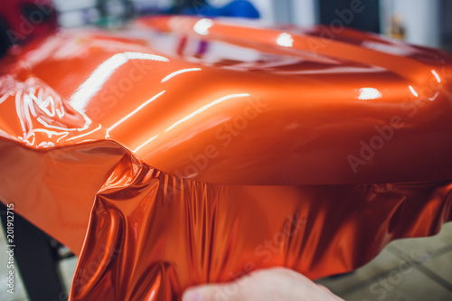 Car wrapping specialist putting vinyl foil or film on car wrapping protective film yacht, boat, ship, car, mobile home. orange film hand pulls