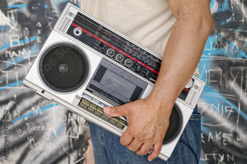 Man holding vintage tape boombox / Man with vintage tape boombox on street at graffiti wall.