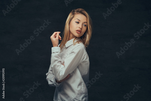 Portrait of a sensual blonde girl dressed in a white shirt, posing in a studio.