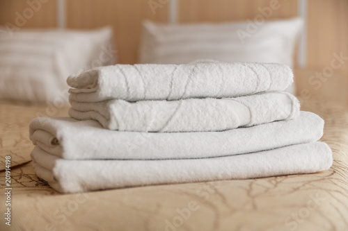 Stack of white hotel towel on bed in bedroom interior. © lizaelesina