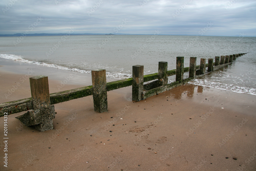 Old wooden groyne on empty, partially covered in sea water on cold overcast day.