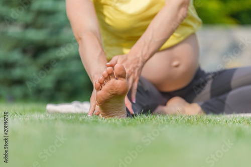 Beautiful pregnant woman in yellow t-shert doing prenatal yoga on nature outdoors. Sport, fitness, healthy lifestyle.