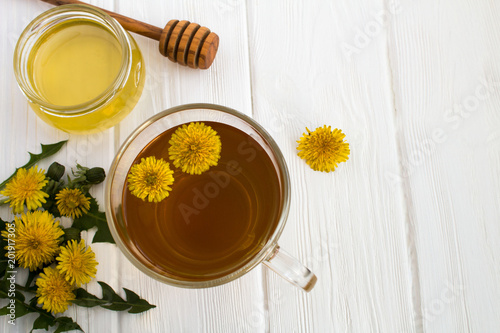 Tea with  dandelions in the glass cup on the white wooden background.Top view.