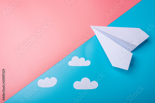 White paper origami airplane with clouds lies on pastel blue background