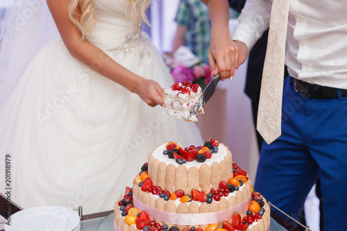 Wedding cake with berries. Bride and groom cut sweet cake on banquet in restaurant.