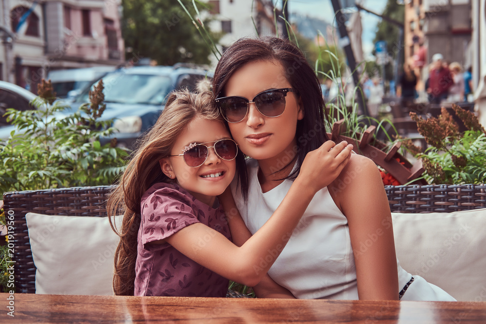 Portrait of fashionable mom and her lovely daughter during a time in an outdoor cafe. Portrait of fashionable mom and her lovely daughter during a time in an outdoor cafe.
