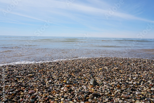 Water washing on shoreline over pebbles on beach on bright sunny day