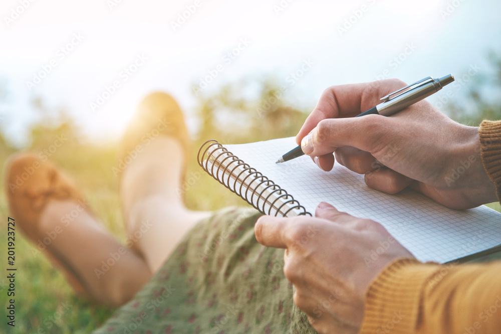 Naklejka premium female hands with pen writing on notebook on grass outside