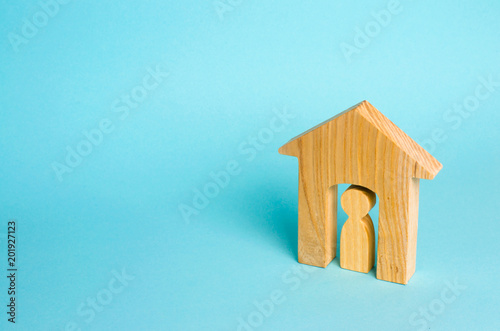 Wooden figurine of a man in a house on a blue background. The concept of an apartment house, real estate. Buying and selling apartments, affordable housing for young families. Protection of rights.