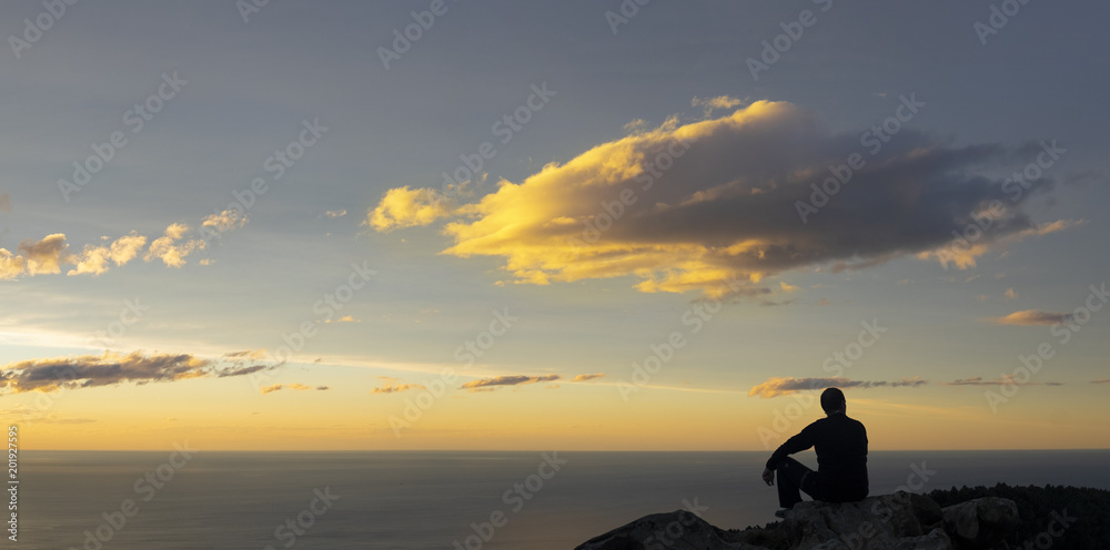 Man sitting by the sea watching the sunset