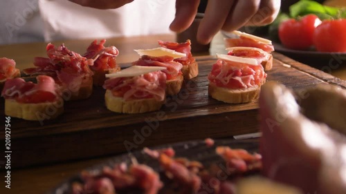 The work of a professional chef for the preparation of traditional Spanish tapas. Unfolding cheese plates on a layer of tomato and bacon.