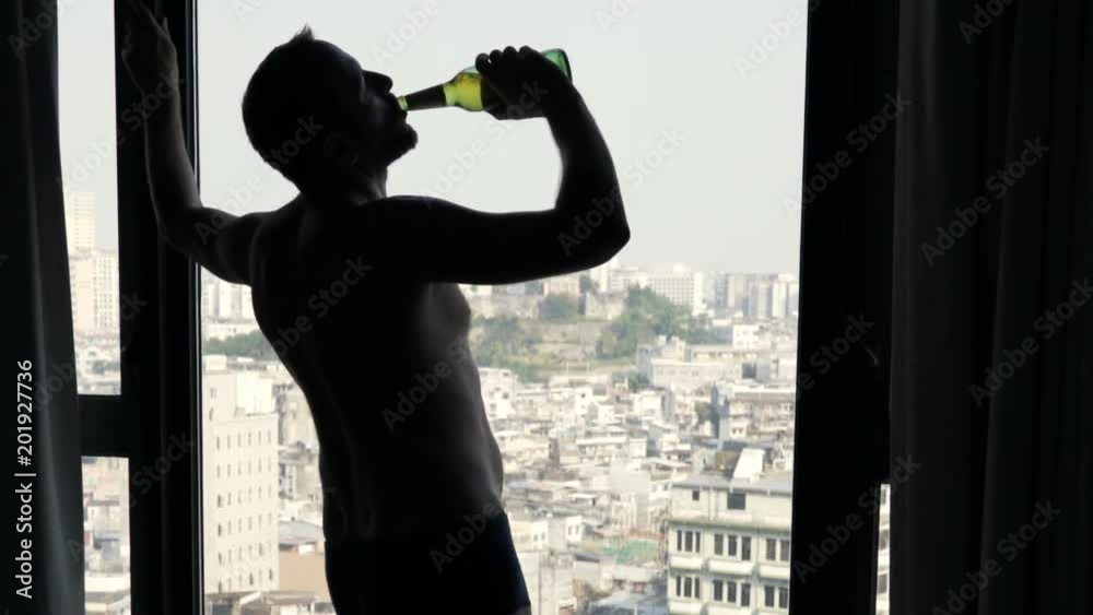 Silhouette of drunk man drinking wine standing by window at home
