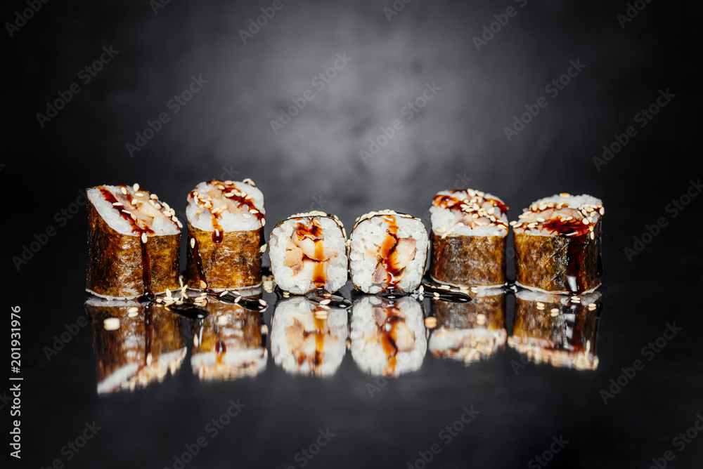 Sushi roll Uguri on dark background made of Nori, Pickled rice, eel / perch Unagi, Unagi sauce, Sesame white. Traditional Japanese cuisine. Sushi menu. Japanese food. Free-space Close-up Sushi roll Uguri on dark background made of Nori, Pickled rice, eel / perch Unagi, Unagi sauce, Sesame white. Traditional Japanese cuisine. Sushi menu. Japanese food. Free-space Close-up