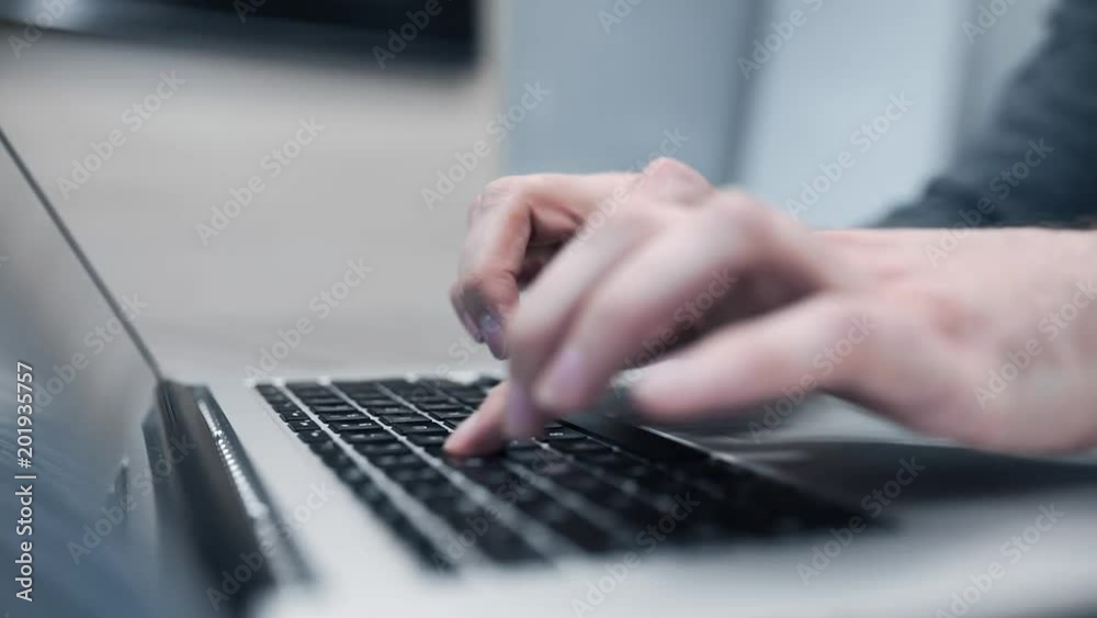 Man in gray pulloverworks at his notebook, man's hands type on the keyboard, man uses notebook, close up of hands with notebook, searching the internet, social media, e-commerce and buisness Man in gray pulloverworks at his notebook, man's hands type on the keyboard, man uses notebook, close up of hands with notebook, searching the internet, social media, e-commerce and buisness