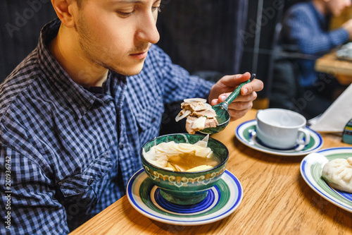 Man eating traditional asian soup from patterned wooden plate