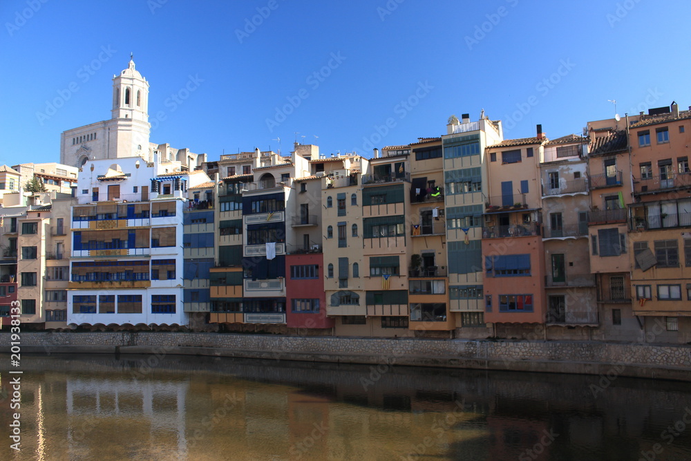 Colorful houses placed close to the Onyar River with amazing cathedral's main tower on backwards, Girona, Spain.
