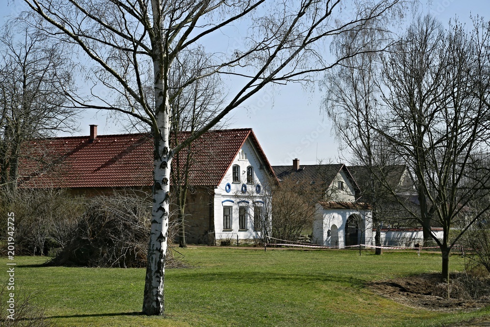 Serec, Czech Republic / Europe - April 7 2018: Village square with white decorated houses, birches and green grass on sunny day, blue sky