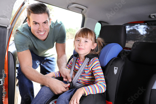Man fastening his daughter with car safety belt