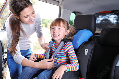 Woman fastening her daughter with car safety belt