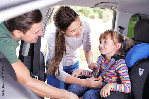 Parents fastening their daughter with car safety belt