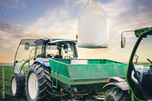 driver puts a sack of fertilizers on a square tractor trailer in the field in the spring