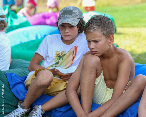 background. two boy friends sit in a green park on a blue soft sofa