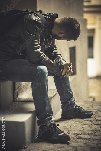Young depressed man sitting in the dark alleyway, feeling sadness and pain