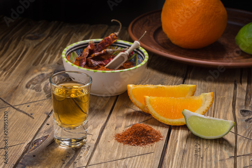Mezcal - traditional Mexican drink with orange and lime slices, chili papper and worm salt on a old wooden table. photo