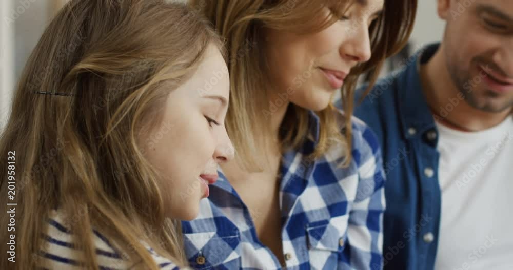 Close up of the nice happy family of parents and two kids sitting close to each other and looking at something with smiles. Indoor Close up of the nice happy family of parents and two kids sitting close to each other and looking at something with smiles. Indoor