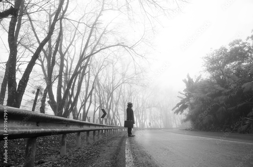 Traveler asian man with a long coat in foggy misty road Traveler asian man with a long coat in foggy misty road