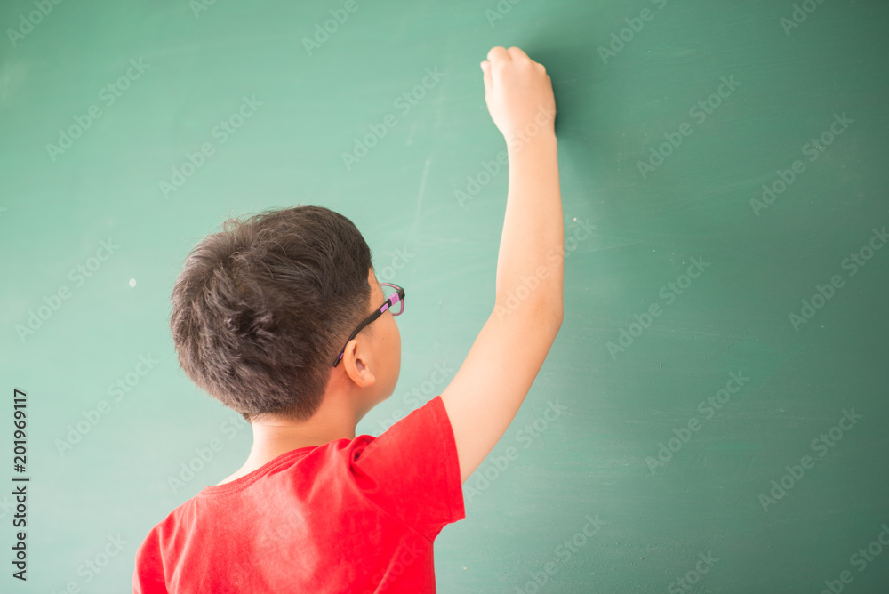 Little asian boy writing on empty green board at school