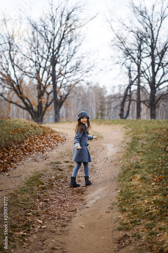 A cute girl in gey coat and gray hat in the oak wood in autumn walking at the sunset
