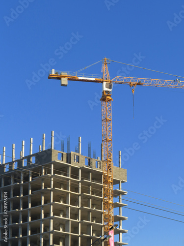 Close-up of a crane with a house under construction on the background of beautiful blue sky with clouds.