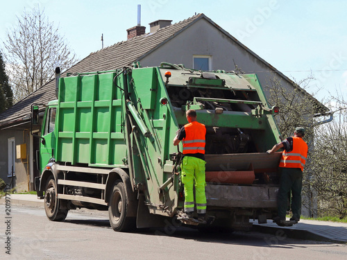 Carriage of garbage by the municipal service. Two janitors load garbage into the garbage truck. Ecology and cleanliness of the city. Utilization of municipal waste Manual workers. Cleaning of the city