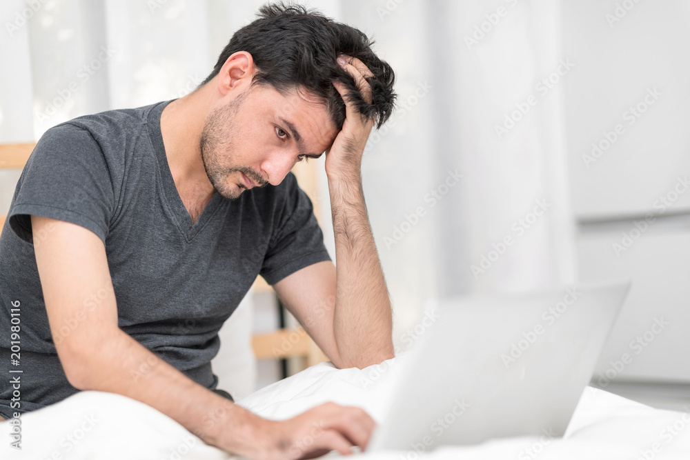 Portrait of Heavy-Hearted Man Looking On Laptop Computer In Bedroom While Massaging His Head. Miserable Unemployed Male Worrying After Checking An Email Showing His Nervousness. Feeling exhausted. Portrait of Heavy-Hearted Man Looking On Laptop Computer In Bedroom While Massaging His Head. Miserable Unemployed Male Worrying After Checking An Email Showing His Nervousness. Feeling exhausted.