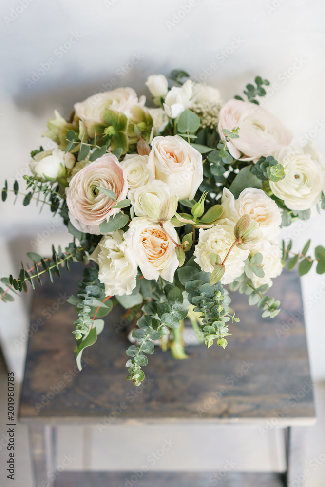 Wedding bouquet of white roses and buttercup on a wooden table. Lots of greenery, modern asymmetrical disheveled bridal bunch