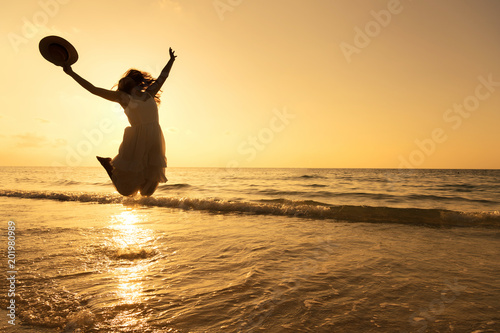 Silhouette of pretty woman wear white dress is jumping and relax on beach. Positive emotions. Summer concept.