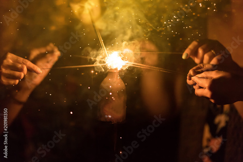 Blurred of Sparklers with group of friends having fun for celebration and hand holding a burn sparkler light and playing together. Cinema film tone with grain.Dark concept.
