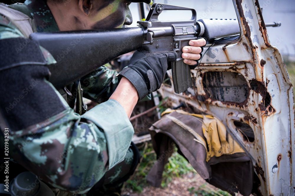 Special forces soldier or private military holding gun aiming behind a dilapibated car at field area. Special forces soldier or private military holding gun aiming behind a dilapibated car at field area.