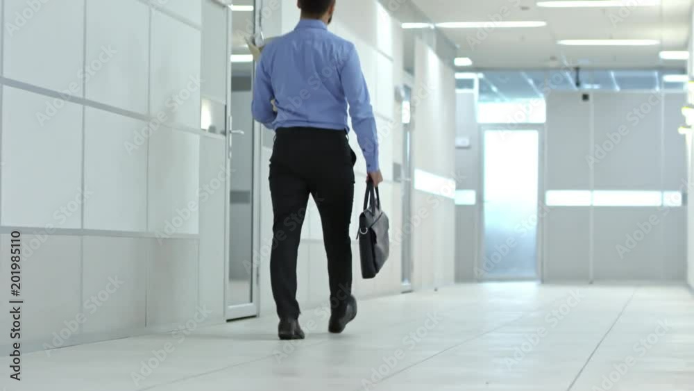 Rear view of businessman walking through hallway with briefcase and carrying personal belongings to new office Rear view of businessman walking through hallway with briefcase and carrying personal belongings to new office