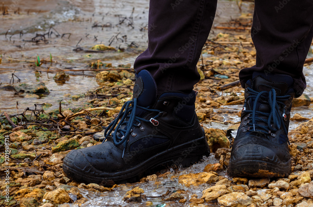 A lonely man in dark jeans and heavy road boots on lacing strolls in the cold season stands on the river bank. On the shore, small stones, ice, thickets of reeds and shrubs. A lonely man in dark jeans and heavy road boots on lacing strolls in the cold season stands on the river bank. On the shore, small stones, ice, thickets of reeds and shrubs.