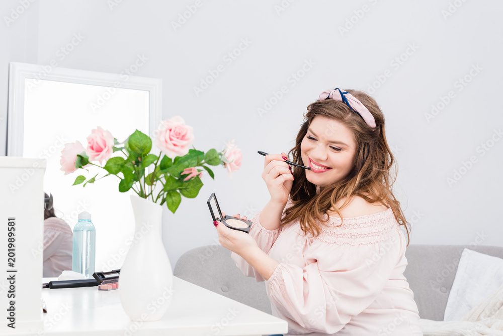 pretty smiling young woman applying lip gloss while doing makeup at home pretty smiling young woman applying lip gloss while doing makeup at home