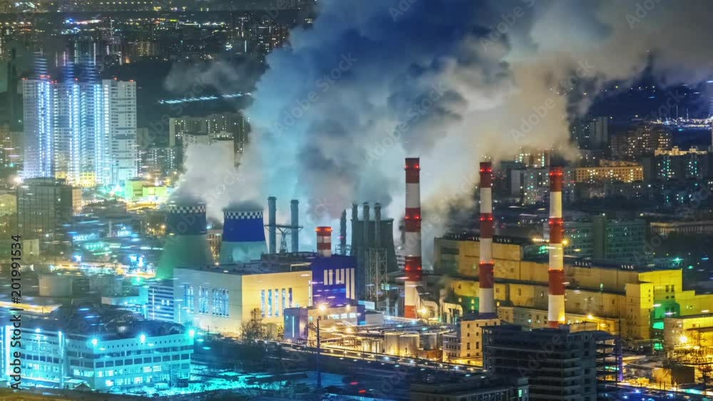 Zoom in on power plant emitting smoke from smokestacks over night city ...