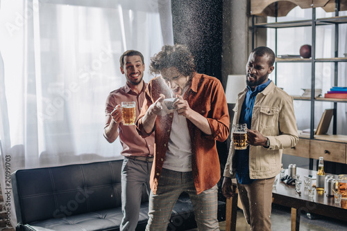 laughing multiethnic friends looking at man drinking beer from can