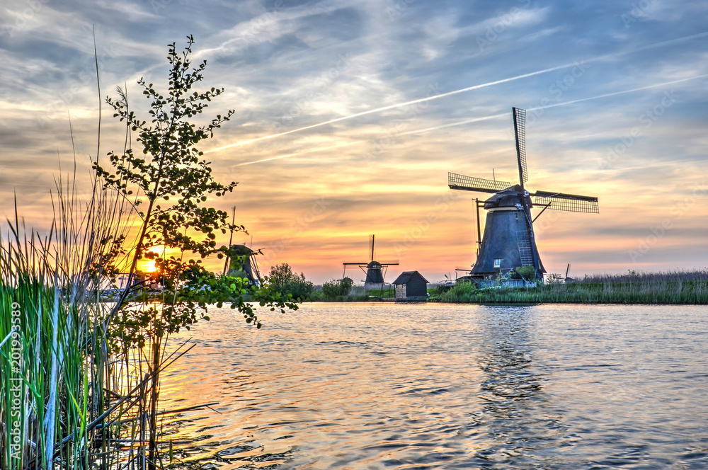 Low sun in a sky with cirrus clouds and contrails over a scene with windmills and a canal at Kinderdijk Unesco world heritage site