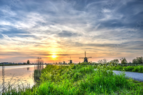 Grassy bank of a canal with in the background the windmills at Kinderdijk Unesco world heritage site under a picturesque evening sky with cirrus clouds