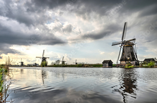 Partially cloudy sky and several historic windmills relfecting in a canal at Kinderdijk Unesco world heritage site