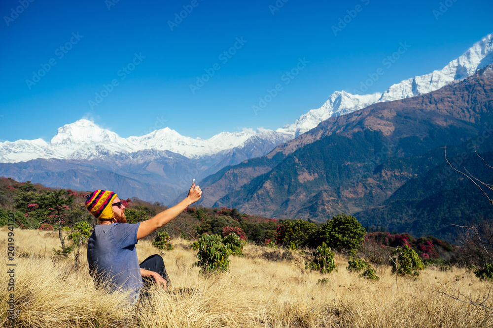 A young man with a red beard and a backpack in the mountains makes a selfie. the concept of active recreation and tourism in the mountains. Nepal in the spring